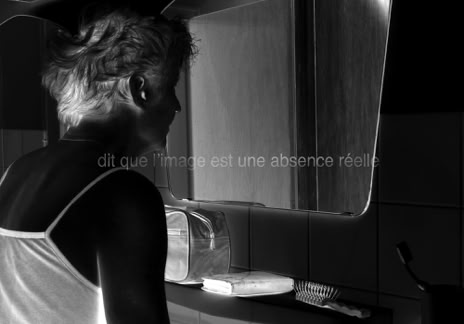 Série métaphysiquée - dit que l'image est une absence réelle, photographie de Jean pierre Morcrette. Photo en négatif noir et blanc de la tête et du torse d’une femme vue de profil, devant un miroir de salle de bain. Sur une étagère se trouvent des accessoires, trousse, brosse à cheveux, etc. On ne voit pas le reflet de la femme dans le miroir. Une ligne de texte est visible en surimpression au centre de l’image : dit que l'image est une absence réelle