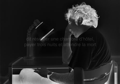Série métaphysiquée, dit réserver une chambre d’hôtel, payer 3 nuits et attendre la mort, photographie Jean pierre Morcrette. Photo en négatif noir et blanc d’un homme assis à une table avec une lampe allumée, tenant sa tête du bras droit. L’autre, dont on voit la montre, est posé sur sa jambe. Deux lignes de texte sont visibles en surimpression au centre de l’image : dit réserver une chambre d’hôtel, payer 3 nuits et attendre la mort