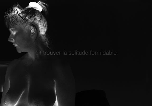 Série métaphysiquée - dit trouver la solitude formidable, photographie de Jean pierre Morcrette. Photo en négatif noir et blanc de la tête et du torse d'une femme vus de profil, à la poitrine nue, avec des cheveux attachés, sur un fond sombre. Une ligne de texte est visible en surimpression au centre de l’image : dit trouver la solitude formidable